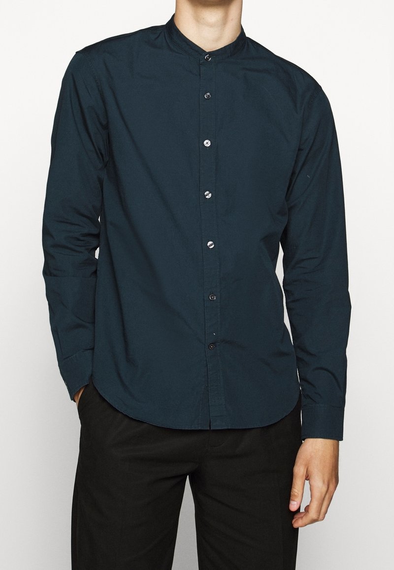 Ciemnoniebieska, długosleeve'owa koszula z kołnierzykiem stojącym, z przodem na guziki i gładką bawełnianą teksturą. Dopasowany krój z zaokrąglonym dołem.
