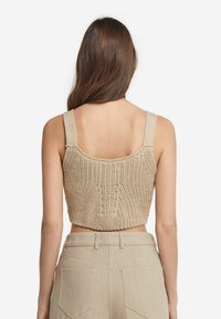 Strickad crop top i beige med breda remmar och ett strukturerat mönster, i kombination med högmidjade beige byxor med bakfickor.