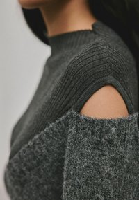 Grauer Strickpullover mit gerippter Textur, hochgeschlossenem Kragen und cut-out Schultern, aus weichen Materialien für einen gemütlichen Sitz.