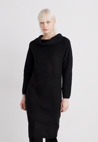Abito lungo a maniche lunghe in maglia nera con scollatura a cascata, silhouette dritta e texture morbida; arriva sotto il ginocchio, design minimale, senza motivi o dettagli.