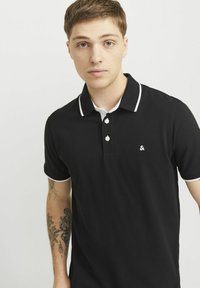 Zwarte poloshirt met witte kraag en mouwaccenten, voorzien van een klein logo op de borst en een knoopsluiting.