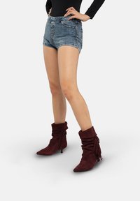 Bordeauxrode suède enkellaarsjes met een nonchalant ontwerp, spits toelopende neuzen en franjes, gecombineerd met denim shorts.