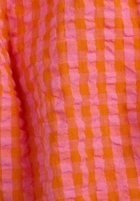 Tessuto con un motivo a scacchi composto da quadrati alternati di colore rosa e arancione. Il tessuto è leggero e leggermente testurizzato.