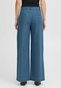 Wijdvallende denim broek in donkerblauw, met twee achterzakken, nette lijnen en een hoge taille. Soepele textuur en een getailleerde pasvorm.