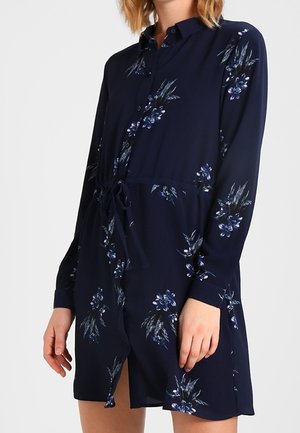 Robe bleue marine à boutons avec un motif floral dans des tons de bleu et de vert, dotée de manches longues et d'une taille ajustable grâce à un lien.