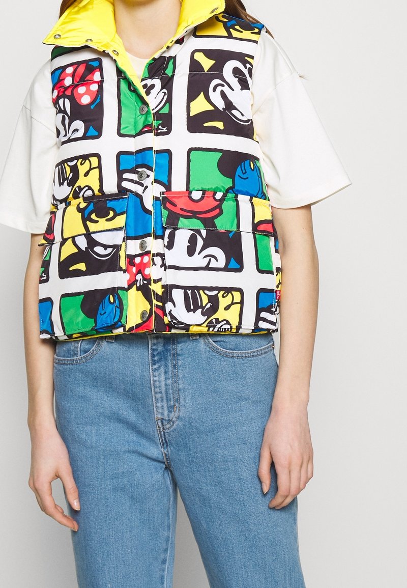 Doudoune sans manches colorée avec un imprimé graphique de Mickey Mouse, principalement en bleu, vert, jaune, noir et rouge. Col jaune, boutons pression.