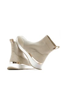 Béžové pletené kotníkové boty s texturovaným vzorem včelí plástve, kovovým akcentem na podrážce a poutkem na zadní straně pro snadnější obouvání.