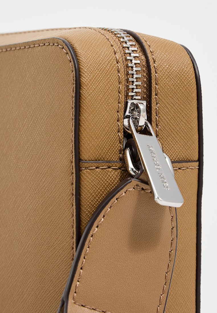 Sac zippé beige en matériau synthétique texturé, doté de quincaillerie argentée et d'une étiquette. Une couture borde les bords, créant un contraste.