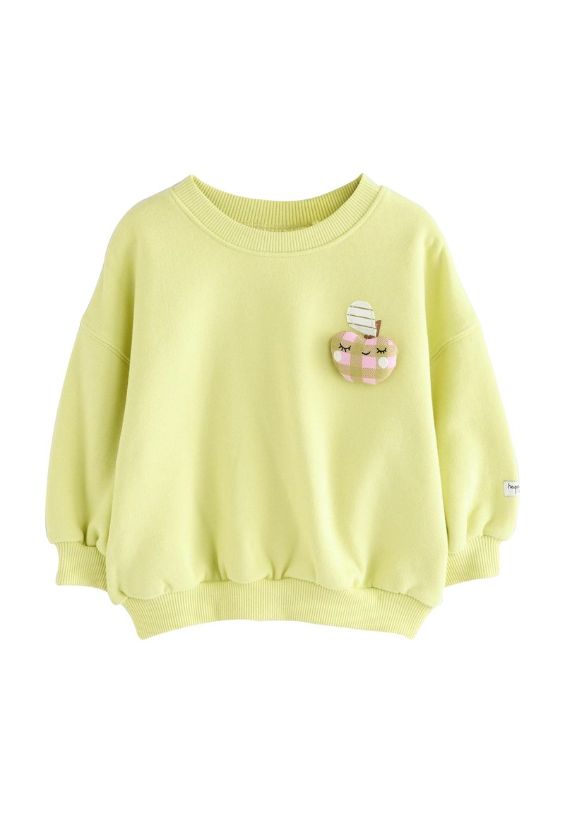 Light yellow sweatshirt with a relaxed fit, ribbed neckline and hem. Features a whimsical embroidered patch of a smiling apple with stripes.