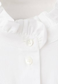 Gros plan d'un col de chemise blanc avec un bord froncé et deux boutons blancs attachés sur un tissu lisse.