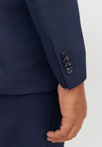 Ärmel eines marineblauen Blazers mit strukturiertem Design, glatter Textur und vier schwarzen Knöpfen mit detaillierter Stickerei entlang des Bündchens.