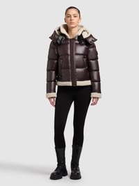 Bruine pufferjas met een beige fleece capuchon, gekenmerkt door een korte snit, doorgestikt design en zwarte hardware accenten. Draagt zwart legging en laarzen.