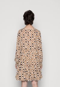 Vestido de manga larga con un patrón geométrico en beige, marrón y blanco. Presenta un dobladillo de capas y puños elásticos. Se muestra la vista trasera.