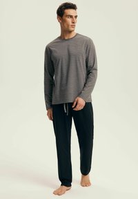 Grau gestreiftes Langarmoberteil mit rundem Ausschnitt, kombiniert mit schwarzen Jogginghosen mit Kordelzug. Der Stoff wirkt weich und leicht.