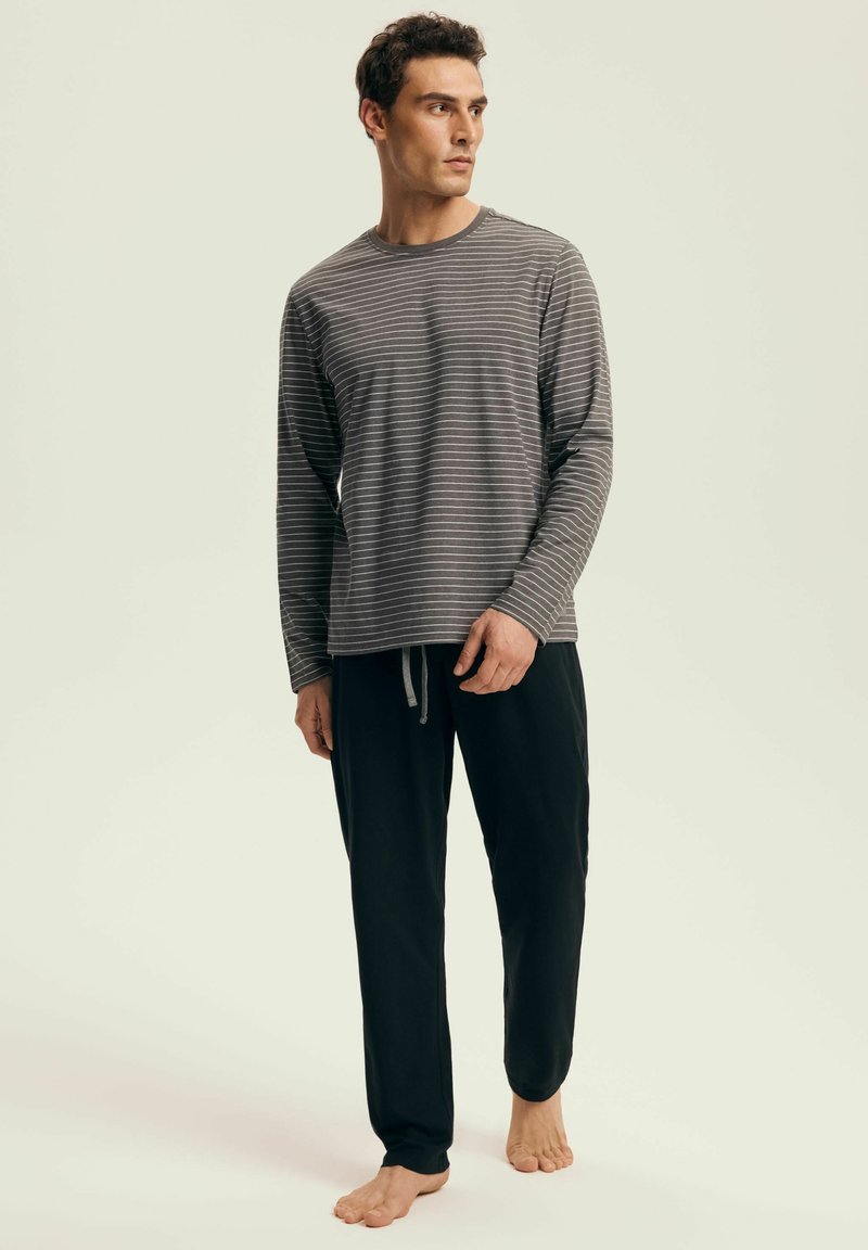 Grau gestreiftes Langarmoberteil mit rundem Ausschnitt, kombiniert mit schwarzen Jogginghosen mit Kordelzug. Der Stoff wirkt weich und leicht.