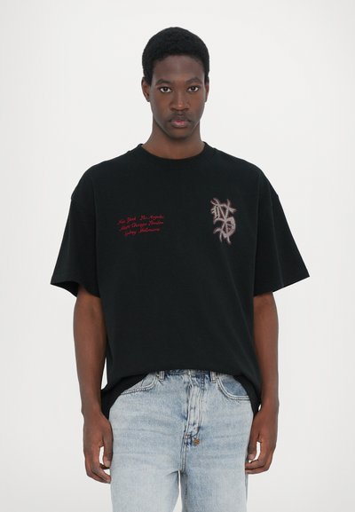 Černé oversized tričko s krátkými rukávy, s vyšitým červeným textem a texturovaným designem na levé straně.