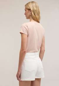 Helles rosa T-Shirt mit kurzen Ärmeln und gerippten Akzenten an den Schultern, kombiniert mit weißen, hoch sitzenden Denim-Shorts mit Gesäßtaschen und fransigem Saum.