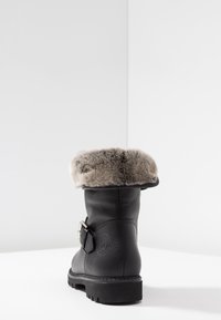 Black leather ankle boot with a faux fur cuff, silver buckle accent, textured sole, and rounded toe. Minimalist design with subtle branding.