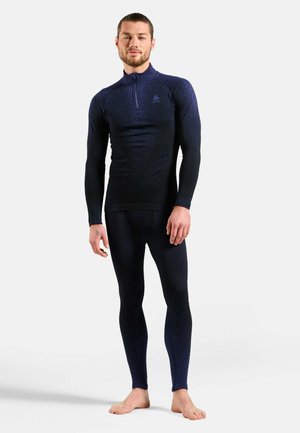 Navy-blaues Langarmshirt mit halbseitigem Reißverschlusskragen und strukturiertem Stoff, kombiniert mit passenden, figurschmeichelnden Leggings. Beide Teile zeichnen sich durch ein elegantes Design aus.