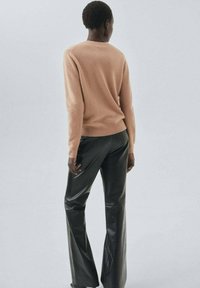 Licht perzik, gestructureerde gebreide trui gecombineerd met zwarte, flare, faux leren broek. De outfit benadrukt een strakke silhouet en een eigentijdse stijl.