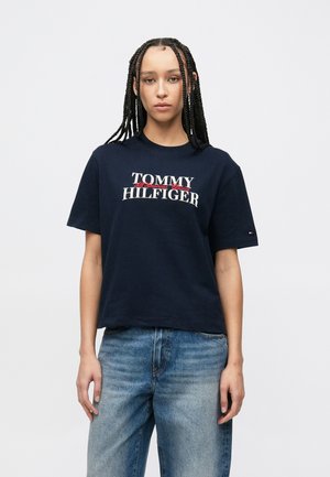 Tumši zils kokvilnas T-krekls ar logotipu "TOMMY HILFIGER" baltā un sarkanā krāsā, īsām piedurknēm, brīvā piegriezumā, uz piedurknes ir neliela karoga emblēma.