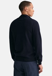 Marine blauwe gebreide trui met een zachte textuur, voorzien van een kraag, geribbelde mouwen en zoom. Van achteren weergegeven, gecombineerd met donkere broeken.