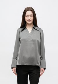 Siva satenska bluza s V-izrezom i ovratnikom, s dugim rukavima i opuštenim krojem. Glatka tekstura i minimalistički dizajn.