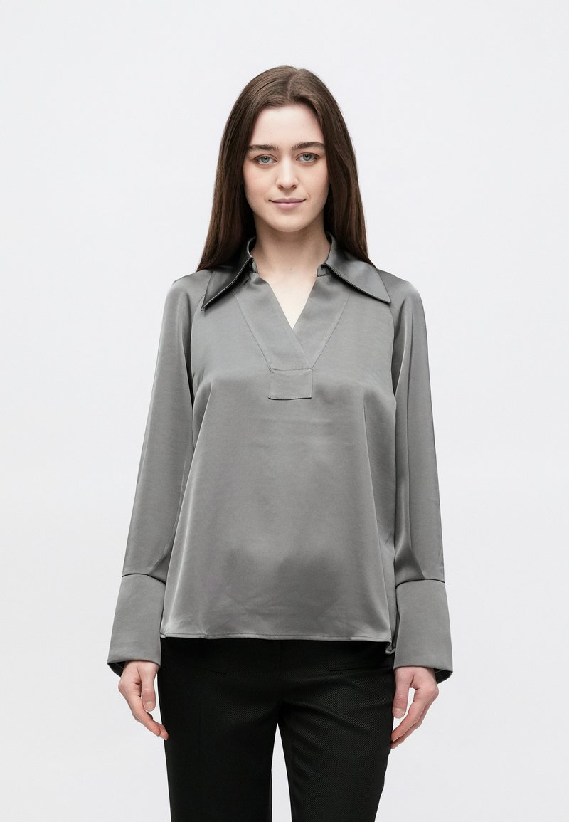 Siva satenska bluza s V-izrezom i ovratnikom, s dugim rukavima i opuštenim krojem. Glatka tekstura i minimalistički dizajn.