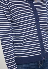 Námořnická modrá a bílá pruhovaná cardigan s kulatým výstřihem, zapínáním na knoflíky a žebrovaným lemem; měkká, lehká tkanina.