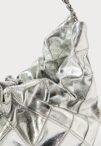 Σακούλα από τσαλακωμένο μεταλλικό ασημένιο δέρμα με ορατές ραφές και ασημένια πλεκτή αλυσίδα ως χερούλι σε φωτεινό φόντο.