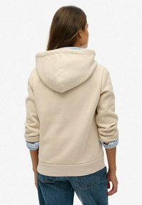 Beige hoodie met geribde manchetten en zoom, met een gladde textuur en een gelaagde look met een blauw geruit overhemd eronder.