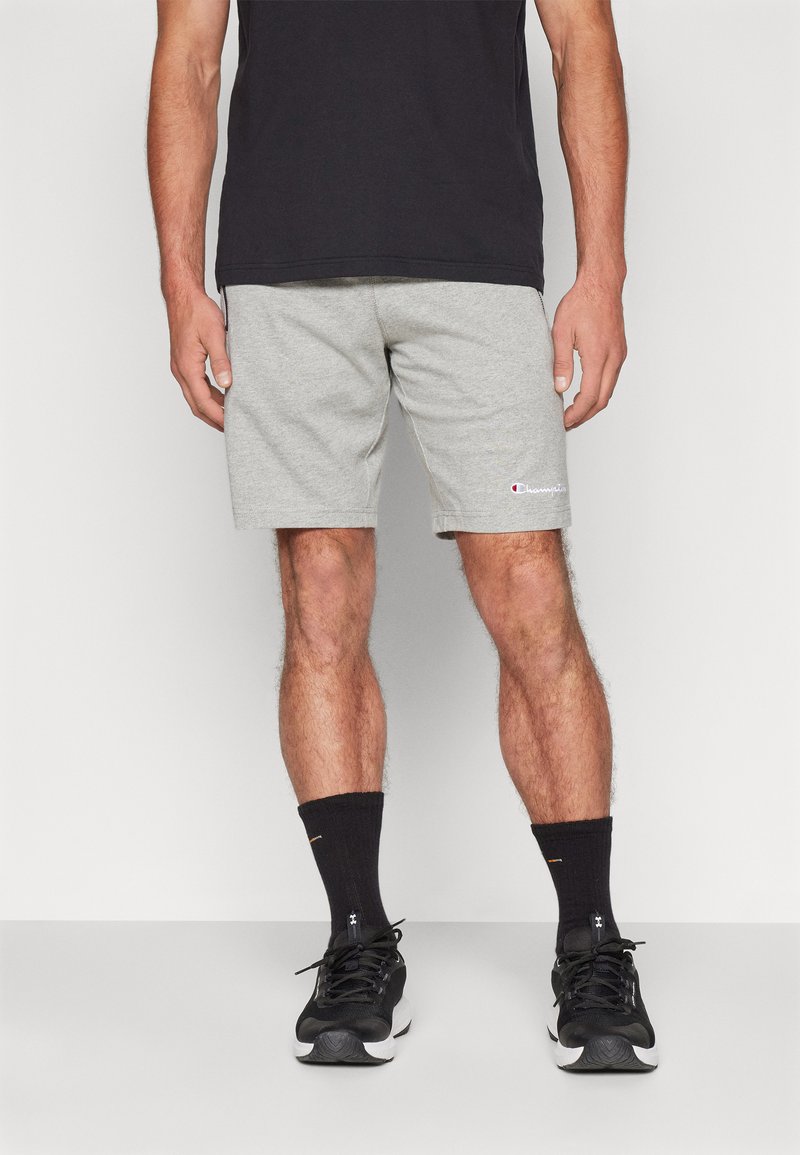 Pantalones cortos deportivos grises hechos de una mezcla de algodón, con una cintura elástica y un logo bordado. Combinados con calcetines negros y zapatillas deportivas.