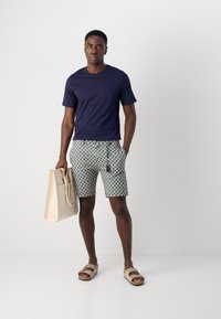 Marineblauw T-shirt, korte broek met een geweven ontwerp in lichte kleuren, beige totebag en casual sandalen. Gladde textuur, relaxte pasvorm.