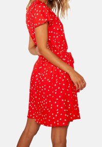 Abito rosso a maniche corte con motivi floreali bianchi, vita aderente e cintura con fiocco. Realizzato in tessuto leggero, design a lunghezza ginocchio.