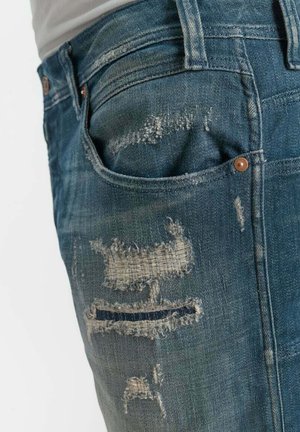 Nahaufnahme von blauen Jeans mit mehreren abgenutzten Stellen und sichtbarer Naht in der Nähe einer Vordertasche.