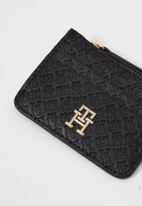 Black textured leather wallet with embossed logo pattern, gold hardware, and zip closure. Compact and sleek design.