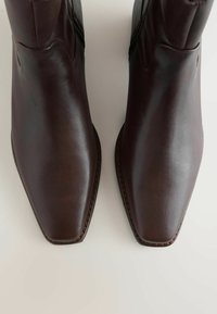 Pair of dark brown leather boots with square toes viewed from above on a plain light surface.