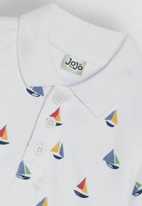 Valge polo särk, millel on mitmevärvilised purjekate mustrid. Sellel on krae, kolm nuppu ja kaeluses "Jojo" silt.