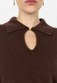 Top de punto marrón con cuello redondo, corte en forma de ojal y acento de perla en el escote. El material es suave con un acabado texturizado.