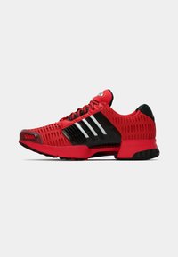 Red athletic shoe with black accents, made of mesh and synthetic materials, featuring three white stripes, textured surface, and a cushioned sole.