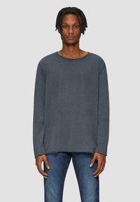 T-shirt en coton gris foncé à manches longues avec un col légèrement arrondi et des détails de couture visibles, porté avec un jean bleu.