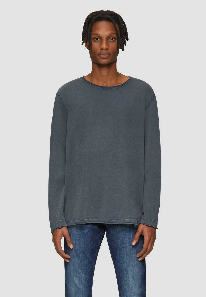 T-shirt en coton gris foncé à manches longues avec un col légèrement arrondi et des détails de couture visibles, porté avec un jean bleu.
