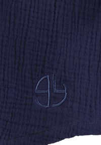 Granatowy teksturowany materiał z okrągłym haftowanym logo w jaśniejszym niebieskim kolorze. Powierzchnia ma marszczony wzór i obszyty brzeg.