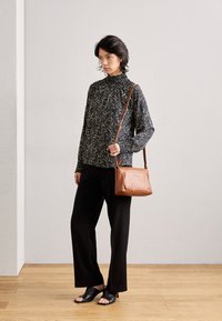 Long-sleeve black top with white speckles, black wide-leg pants, black open-toe slides, and a brown leather crossbody bag.
