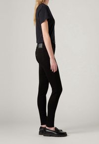 Jeans ajustados negros con una textura suave, cintura de altura media y bolsillos traseros sutiles. Combinados con una camiseta azul marino ajustada y mocasines negros.