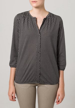 Blouse noire avec un motif géométrique blanc, décolleté en V, détails froncés aux épaules et manches 3/4. Fabriquée en tissu léger.