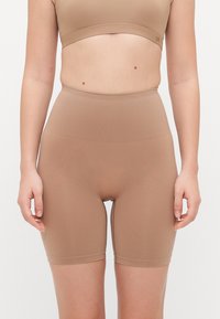 Bodysuit šortsevi u svijetlosmeđoj nijansi, izrađeni od rastezljivog materijala s visokim strukom, glatkom teksturom i uskim dizajnom.