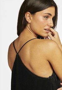 Robe plissée noire avec fines bretelles, mettant en valeur un dos décolleté. Texture lisse accentuée par des rainures verticales et un léger évasement à l'ourlet.