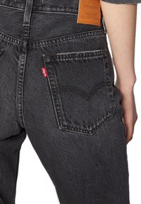 Jeans de mezclilla negra con un bolsillo trasero que presenta un diseño cosido, una etiqueta roja de Levi's y un parche de cuero en la cinturilla.