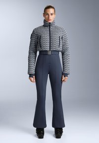 Tamnoplava strukturalna jakna s visokim ovratnikom, uparen s uskim tamnoplavim hlačama s raširenim donjim dijelovima. Crne čizme s sjajnom završnom obradom upotpunjuju izgled.